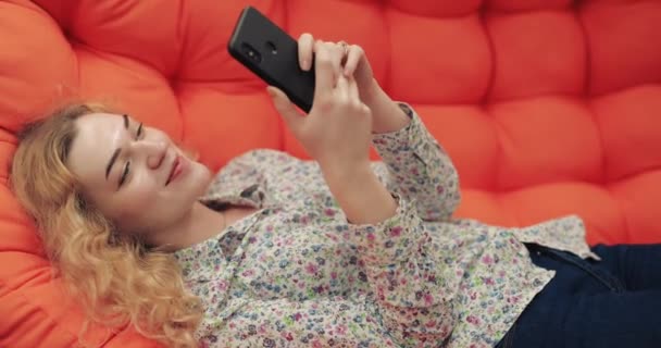 Vrouw met smartphone zittend op oranje bank — Stockvideo