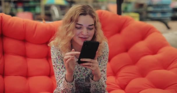 Vrouw met smartphone zittend op oranje bank — Stockvideo