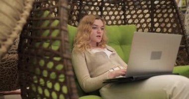 Dizüstü bilgisayarla çalışan bir kadın koza sandalyesinde oturuyor.