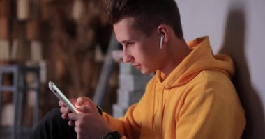 Man in yellow hoodie using smartphone and earbuds at home