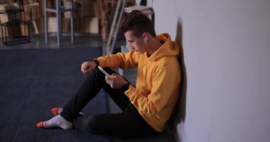 Man in yellow hoodie using smartphone and earbuds at home