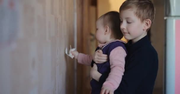 Милая маленькая девочка стирает обои со своим братом — стоковое видео