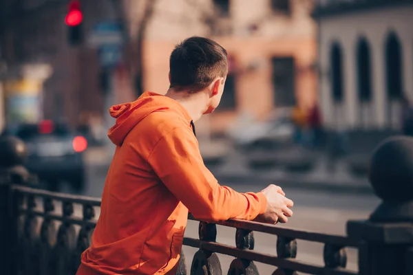 Man in orange clothes standing in city and thinking