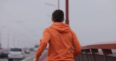 Turuncu kapüşonlu bir adam köprüde koşuyor.