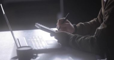 Dizüstü bilgisayarla çalışan serbest çalışan bir adam bir kafede not defterine notlar yazıyor.