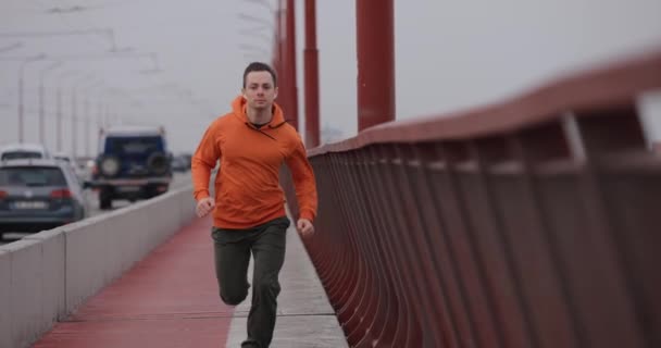 Mann in orangefarbenem Kapuzenpullover läuft schnell auf Brücke, Zeitlupe — Stockvideo