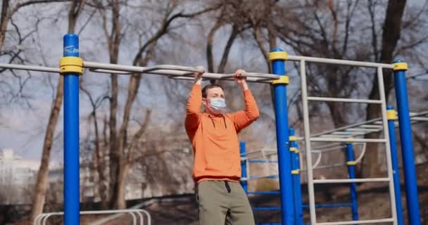 Man pulls up on the bar outdoor in a surgical mask — Stock Video