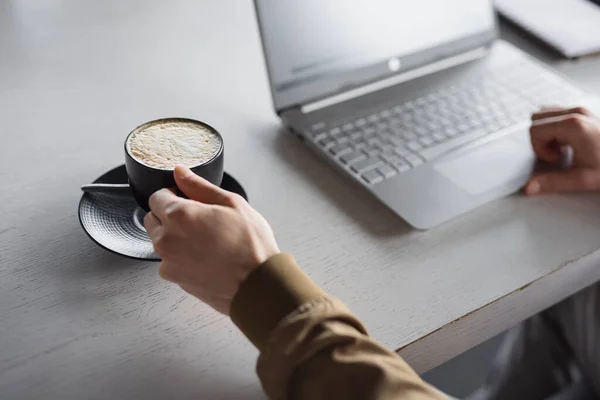 Gros plan mains masculines travaillant sur le clavier d'ordinateur portable prendre une tasse de latte — Photo