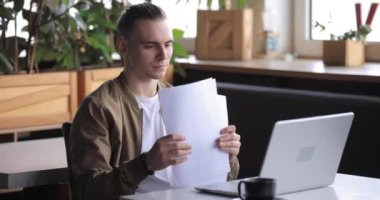 Bir kafede bilgisayar ve kağıtlarla çalışan serbest çalışan bir adam.