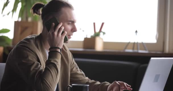 Empresario trabajando por ordenador portátil en un café y hablando por teléfono — Vídeos de Stock