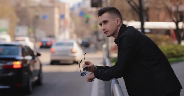 Joven apoyado en barreras mira el tráfico de coches de la ciudad — Vídeo de stock