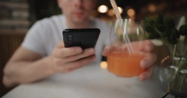 Yakından bakınca restoranda meyve suyu içiyor. Akıllı telefonlara bakıyor.