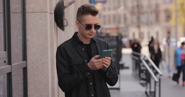 Młody człowiek w okularach przeciwsłonecznych korzystający z telefonu w mieście — Wideo stockowe