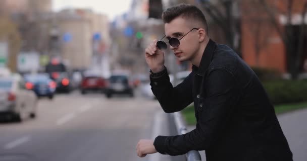 Młody człowiek opierający się na barierkach patrzy na ruch samochodowy w mieście — Wideo stockowe