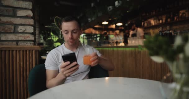 El hombre bebe jugo de frutas en el restaurante mirando en el teléfono inteligente — Vídeo de stock