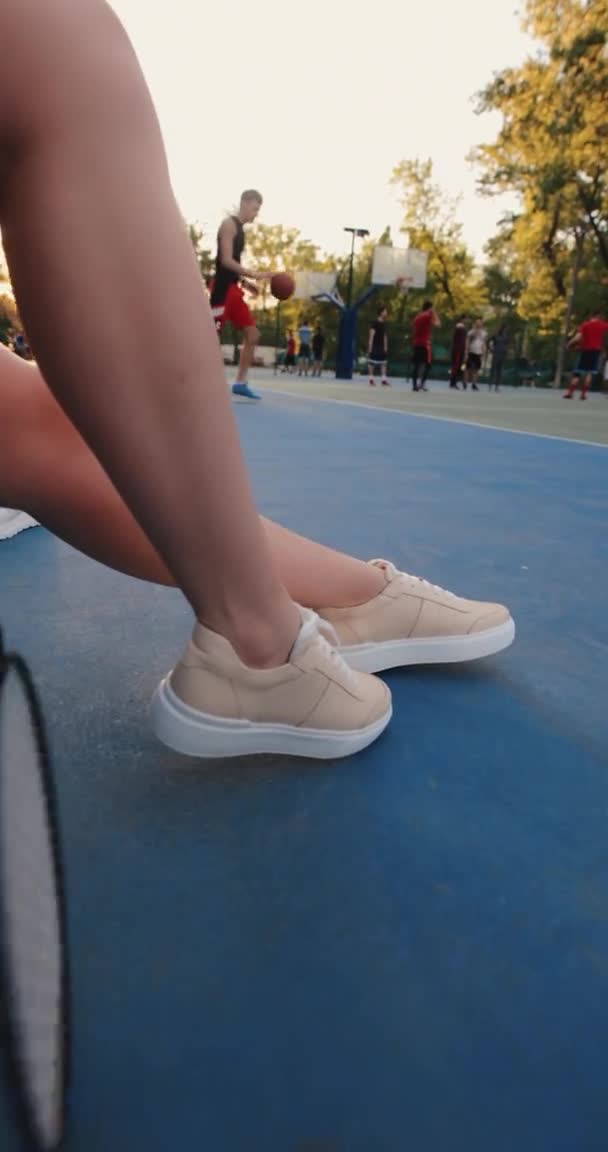 Pernas femininas sentadas em um campo de basquete, vídeo vertical — Vídeo de Stock