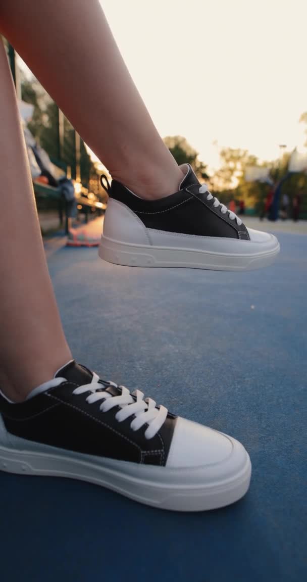 Ženské nohy sedí na basketbalovém hřišti v černých gumových botách, vertikální video — Stock video
