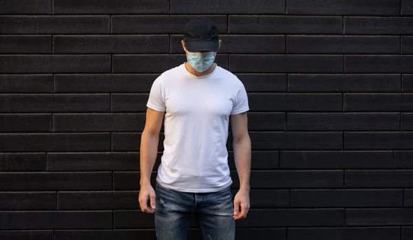 Mies valkoisessa t-paidassa seisoo tiiliseinää vasten, mockup design — kuvapankkivalokuva
