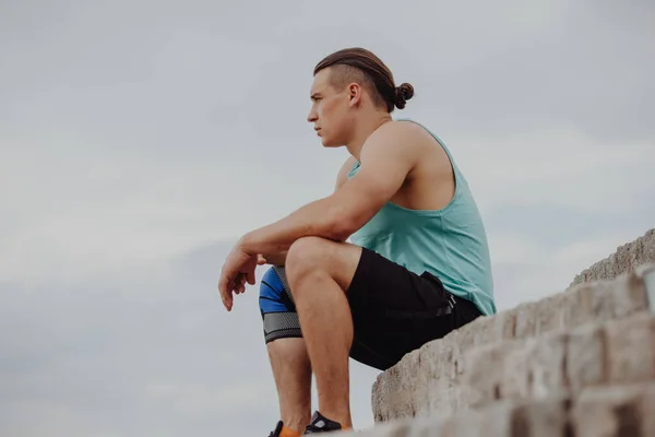 Sporty man sitting and thinking outdoor against a sky background — Stock Photo, Image