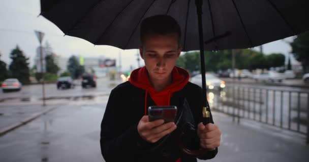 Hombre caminando en la ciudad bajo paraguas usando smartphone — Vídeos de Stock