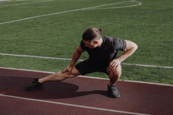 Man stretches leg before running on a stadium — Stock Photo, Image