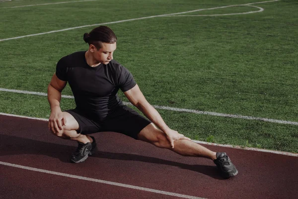 Man stretches leg before running on a stadium — Stock Photo, Image