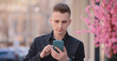 Bir bahar şehrinde cep telefonu kullanan gülümseyen genç adam.