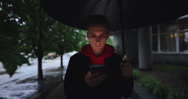 Mężczyzna spacerujący po alejce pod parasolem za pomocą smartfona — Wideo stockowe