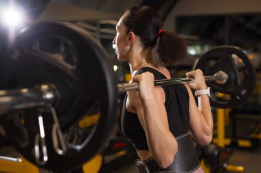 Spor salonunda ağır ağır çömelmiş bir kadın.