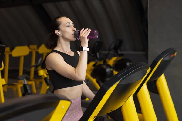 Mulher fitness bebe uma água enquanto corre na esteira — Fotografia de Stock