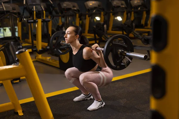 Vrouw hurkt met zwaar gewicht in een sportschool — Stockfoto