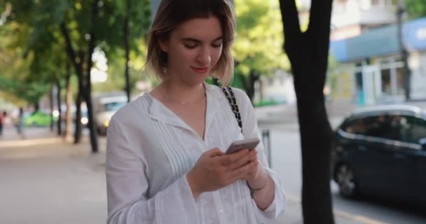 Mensajería de mujer por teléfono móvil caminando en una ciudad de verano — Vídeos de Stock