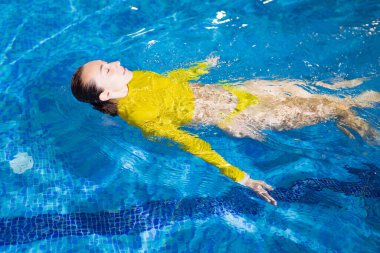 Mutlu, rahat bir kadın kapalı havuzda sırt üstü yüzer.