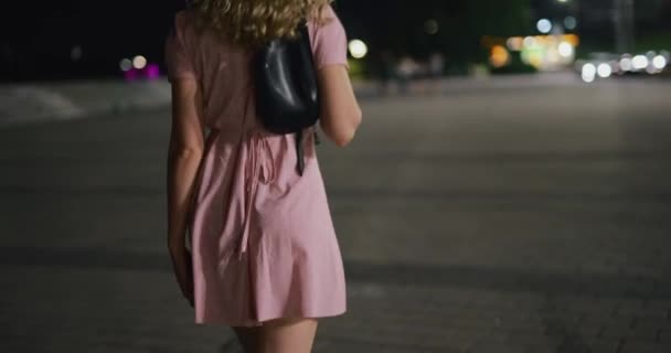 Сексуальная женщина в платье ходит по ночному городу и поворачивается обратно — стоковое видео
