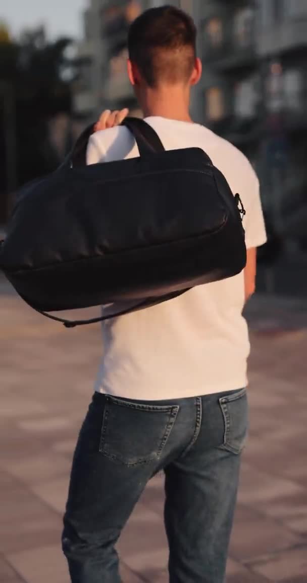 Mężczyzna chodzi po mieście trzymając torbę na ramieniu. — Wideo stockowe