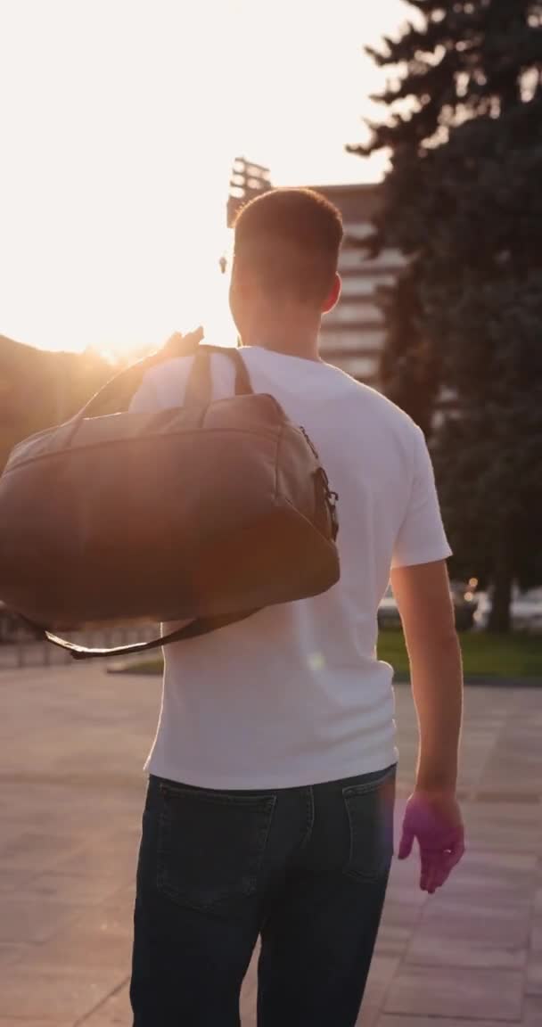 Un hombre camina alrededor de la ciudad sosteniendo la bolsa en su hombro — Vídeos de Stock
