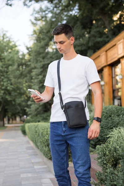 Un hombre camina por la ciudad con una bolsa de mensajero colgante —  Fotos de Stock