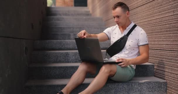 Homem freelancer abrindo e usando laptop sentado nas escadas da cidade — Vídeo de Stock