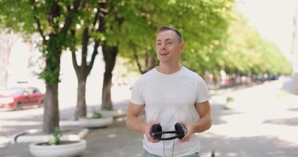 Usmívající se muž nasadí velké sluchátka procházky v letním městě — Stock video