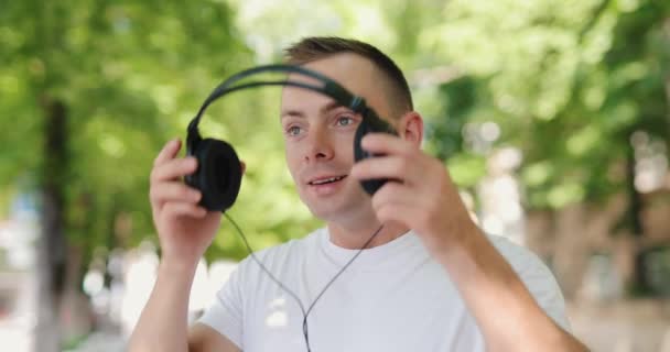 Uśmiechnięty mężczyzna zakłada duże słuchawki w letnim mieście — Wideo stockowe