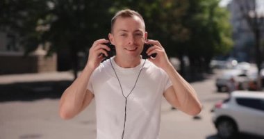 Gülümseyen adam yaz şehrinde büyük kulaklıklar takar.