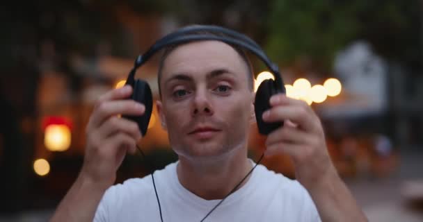 Mann setzt sich in der Abendstadt große Kopfhörer auf — Stockvideo