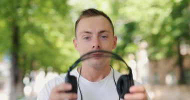 Gülümseyen adam yaz şehrinde büyük kulaklıklar takar.