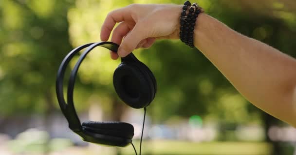 Αρσενικό χέρι κρατώντας μεγάλα ακουστικά σε ένα πάρκο — Αρχείο Βίντεο