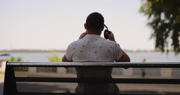 El hombre se pone grandes auriculares sentados en el banco — Vídeos de Stock