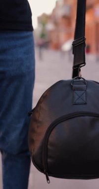 Arkadan bakan adam siyah deri sırt çantasıyla şehirde yürüyor.