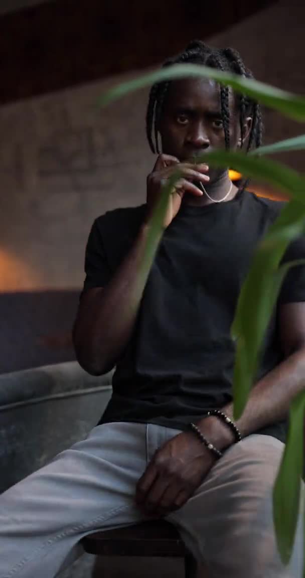 Africano sentado na cadeira com cadeia de cruz cristã em sua boca — Vídeo de Stock