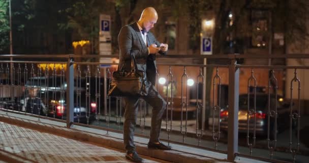 Бизнесмен, использующий смартфон в ночном городе — стоковое видео