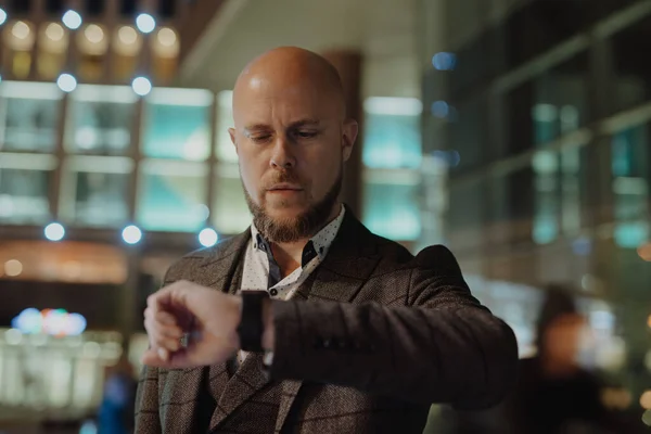 Businessman looks at watch checking a time at night city