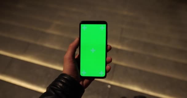 Mano masculina sosteniendo la pantalla verde vacía del teléfono inteligente en la ciudad de la noche — Vídeo de stock